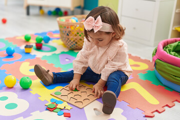Adorable blonde toddler playing with maths puzzle game sitting on floor at kindergarten