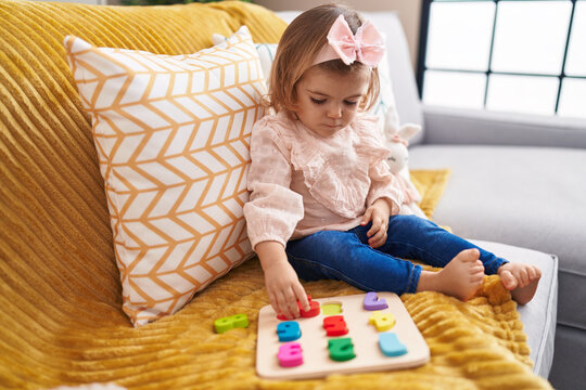 Adorable blonde toddler playing with maths puzzle game sitting on sofa at home