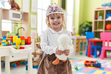 Adorable blonde girl wearing princess crown holding duck toy at kindergarten