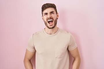 Hispanic man with beard standing over pink background angry and mad screaming frustrated and furious, shouting with anger. rage and aggressive concept.