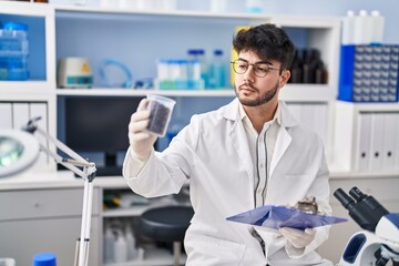 Naklejka na ściany i meble Young hispanic man scientist weighing sample reading document at laboratory