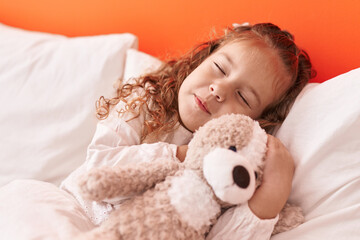 Obraz na płótnie Canvas Adorable blonde toddler hugging teddy bear lying on bed sleeping at bedroom