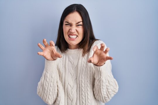 Young brunette woman standing over blue background smiling funny doing claw gesture as cat, aggressive and sexy expression