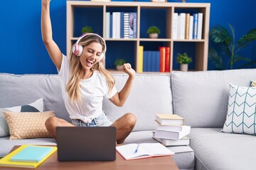 Young blonde woman student sitting on sofa listening to music and dancing at home