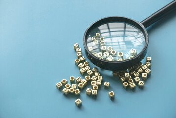 Learning and education concept. Finding keywords. Language learning. Magnifying glass on a bunch of alphabet beads. - obrazy, fototapety, plakaty