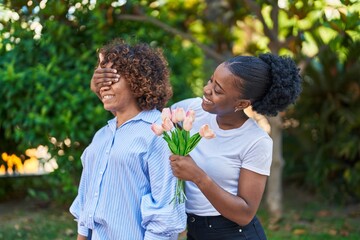 Obraz premium African american women mother and daughter surprise with bouquet of flowers at park