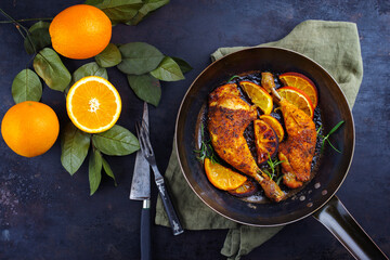 Traditional barbecue chicken drumsticks with orange slices served with herbs as top view on a rustic metal frying pan