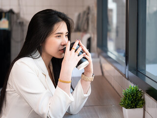 Young beautiful Asian businesswoman smiling and posing while sitting in a modern coffee shop. Young attractive woman sitting in an indoor cafe and looking happy at the camera.