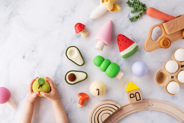 Baby hands with cute wooden and knitting eco toys for activity, motor and sensory development on table top view.