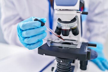 Young beautiful hispanic woman scientist using microscope pouring blood on sample at laboratory