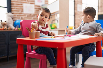 Two kids preschool students sitting on table drawing on paper at kindergarten