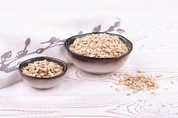 Oat flakes, cereal in handmade ceramic bowls and napkin on white wooden table, rustic style