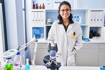 Young latin woman scientist smiling confident standing at laboratory - obrazy, fototapety, plakaty