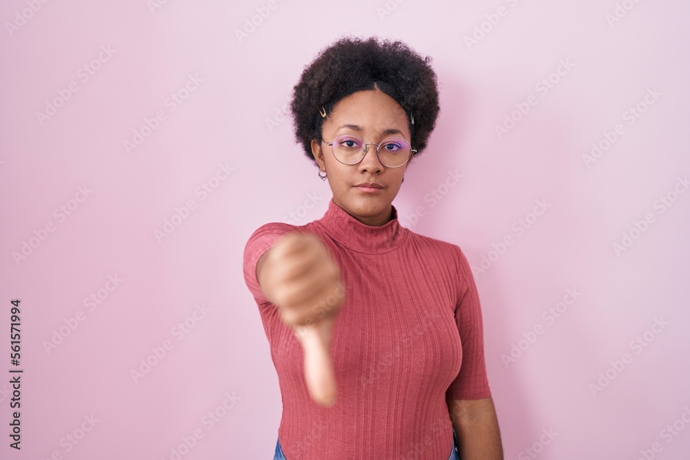 Sticker beautiful african woman with curly hair standing over pink background looking unhappy and angry show