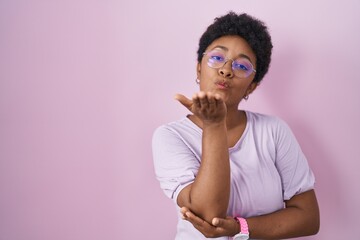 Young african american woman standing over pink background looking at the camera blowing a kiss...
