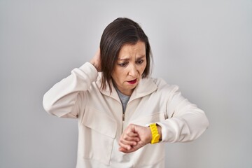 Middle age hispanic woman standing over isolated background looking at the watch time worried, afraid of getting late