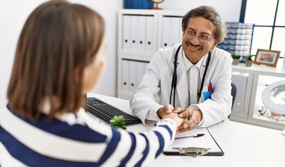 Middle age man and woman wearing doctor uniform having medical consultation holding hand at clinic