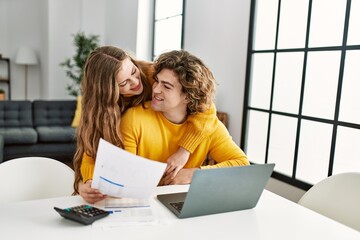 Fototapeta na wymiar Young caucasian couple hugging each other doing family accounting using laptop at home
