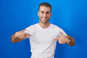 Naklejka premium Young caucasian man standing over blue background looking confident with smile on face, pointing oneself with fingers proud and happy.