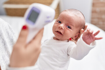 Adorable caucasian baby on mother arms measuring temperature at bedroom