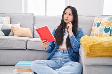 Young chinese woman reading book with doubt expression at home