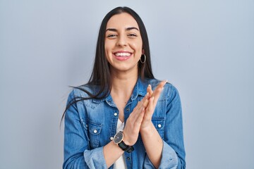 Hispanic woman standing over blue background clapping and applauding happy and joyful, smiling...