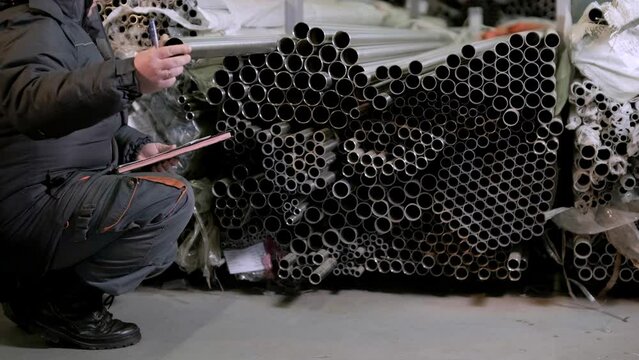 Professional worker in the warehouse of metal products. Factory worker checks the quality of the metal profile