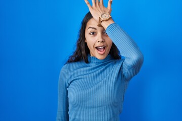 Young brazilian woman standing over blue isolated background surprised with hand on head for mistake, remember error. forgot, bad memory concept.