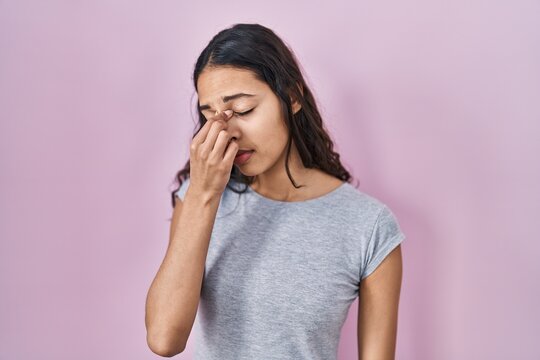 Young brazilian woman wearing casual t shirt over pink background tired rubbing nose and eyes feeling fatigue and headache. stress and frustration concept.