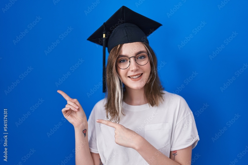 Poster blonde caucasian woman wearing graduation cap smiling and looking at the camera pointing with two ha