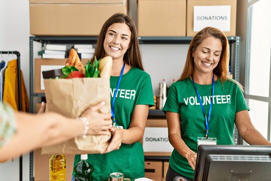 Mother And Daughter Wearing Volunteer Uniform Holding Groceries Paper Bag At Charity Center