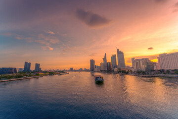 Fototapeta premium Aerial sunset view of Bitexco Tower, buildings, roads, Bason bridge and Saigon river in Ho Chi Minh city, container cargo ship on Saigon river. Travel concept.