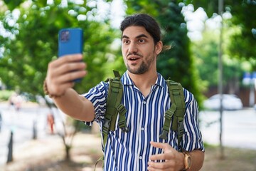 Hispanic man with long hair outdoors at the city doing video call scared and amazed with open mouth...