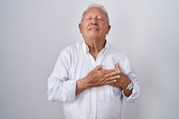 Senior man with grey hair standing over isolated background smiling with hands on chest with closed eyes and grateful gesture on face. health concept.
