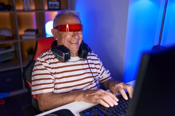 Middle age grey-haired man streamer playing video game using virtual reality glasses at gaming room