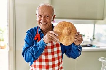 Senior man smiling confident holding homemade bread at kitchen