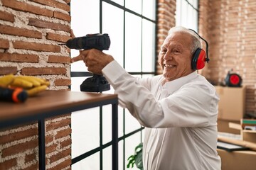 Senior man smiling confident drilling wall at new home