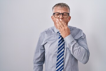 Hispanic business man with grey hair wearing glasses bored yawning tired covering mouth with hand. restless and sleepiness.