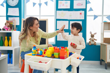 Teacher and toddler playing with construction blocks high five at kindergarten