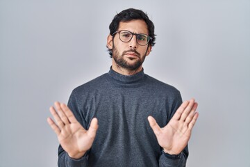 Handsome latin man standing over isolated background moving away hands palms showing refusal and denial with afraid and disgusting expression. stop and forbidden.