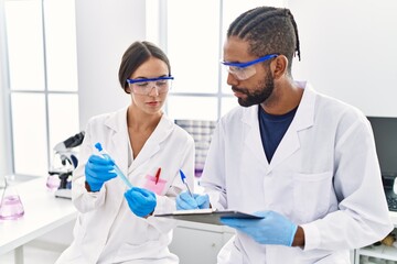 Man and woman scientist partners holding test tube and writing on clipboard at laboratory