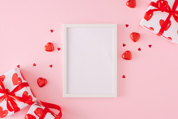 Valentines day concept. Flat lay photo of gift boxes with ribbon, heart shaped chocolate candies, sprinkles on pastel pink background with white frame in the middle. Lovers holiday card idea.