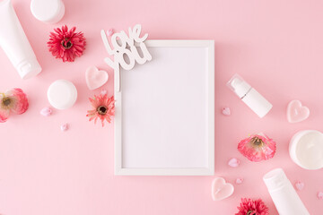 Women day concept. Creative layout made of cosmetic bottles, heart shaped candles, flowers, inscription love you on pastel pink background with white frame in the middle. Mother's day celebration idea