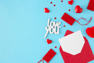 Mothers or women day concept. Top view photo of open red envelope with white card, red hearts, sale tags and inscription love you on pastel blue background with copy space.