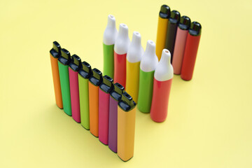 Set of multicolor disposable electronic cigarettes on a bright yellow background.