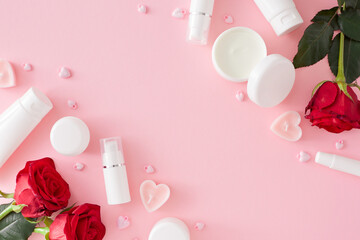 Obraz na płótnie Canvas Mother’s day concept. Flat lay photo of cosmetic bottles without label, red roses and heart shaped candles on pastel pink background with copy space in the middle. Women day cosmetic idea.