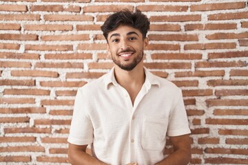 Arab man with beard standing over bricks wall background with hands together and crossed fingers smiling relaxed and cheerful. success and optimistic