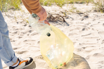 Trash on the beach. Men hand  collects bottle plastic on sea beach. World environment day concept.