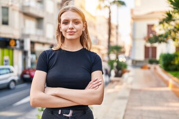 Young blonde woman standing with arms crossed gesture at street