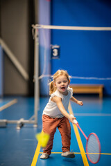 Little girl three years old playing badminton in sport wear on indoor court 